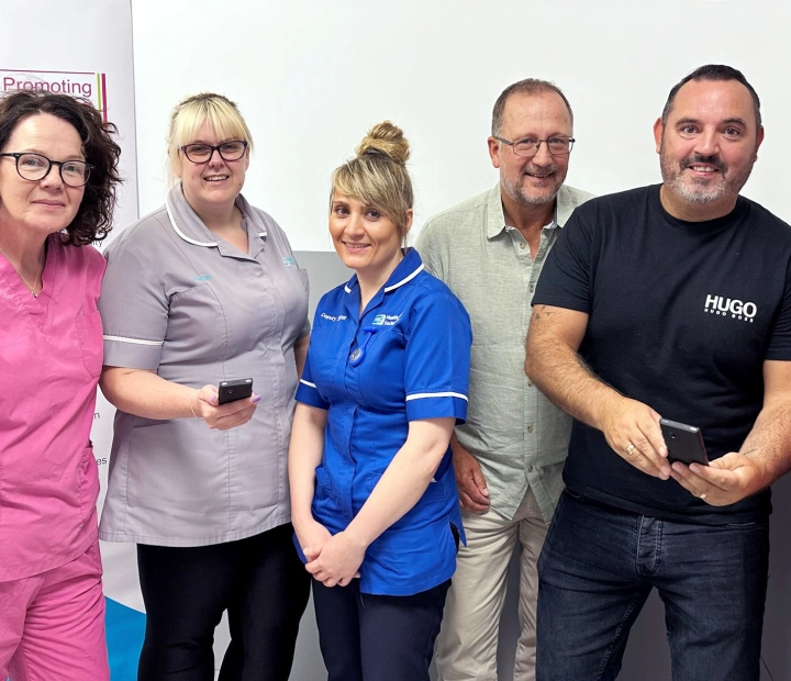 Fem leende personer står tillsammans i sjukvårdskläder, och två av dem håller i en tolk.