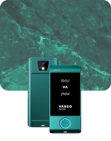 En produktbild som visar en turkosfärgad Vasco Translator-enhet från två vinklar mot en mörk bakgrund av texturerat tyg. Enheten till vänster visar baksidan, där kameralinsen med blixt och det präglade ”VA”-logotypen framhävs. Enheten till höger visar framsidan med upplyst skärm, där hälsningarna ”Hello!”, ”VA”, ”¡Hola!” och ”VASCO Translator”-logotypen visas. En cirkulär knapp längst ned på enhetens framsida är kantad med ett lysande blått ljus. Bakgrunden har ett lyxigt grönt marmormönster med ljusa ådror.